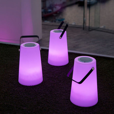 Lampe haut-parleur portable Nómada Blanche en violet avec poignée de transport portable pour l’intérieur et l’extérieur.