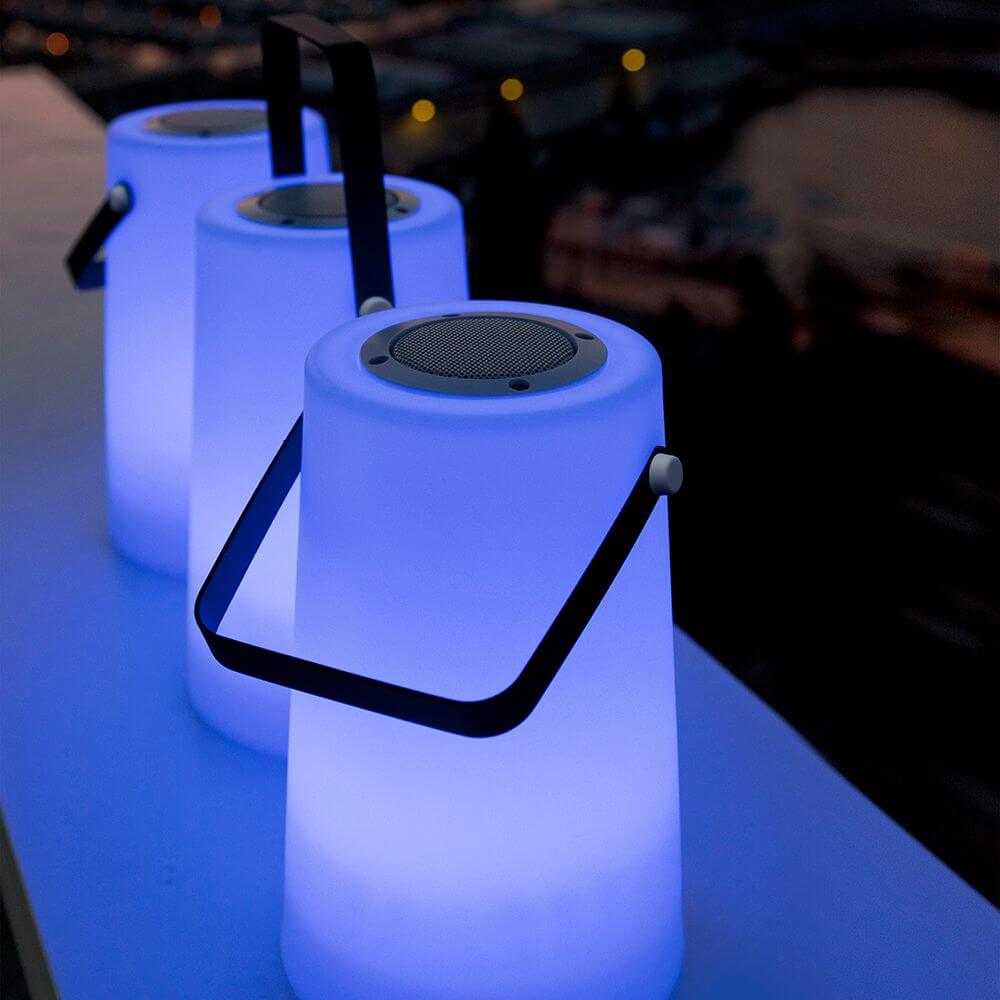 Tragbare Lautsprecher-Leuchte Nómada Weiß mit sanfter Beleuchtung und tragbarem Design auf einem Tisch.
