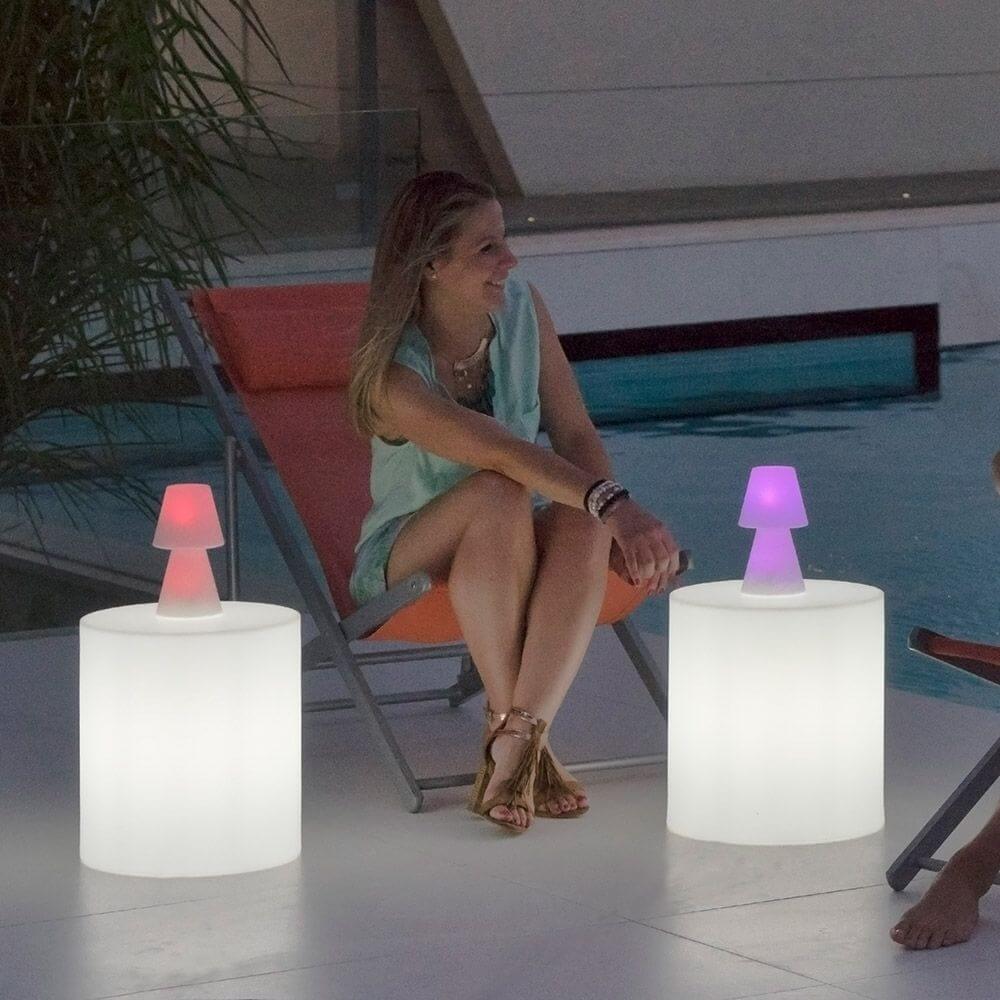 Frau sitzt entspannt neben Lola LED-Außen-Tischleuchten am Pool, stilvolles Ambiente mit buntem Licht.