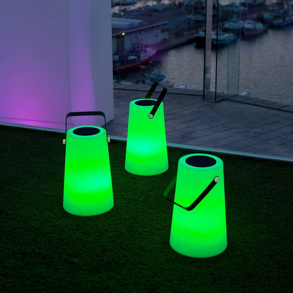 Grüne tragbare Solarleuchten Nómada auf einem Balkon mit Blick auf den Hafen bei Nacht.