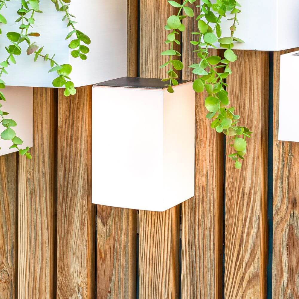 Wally LED Quader-Wandlampe Solar an Holzwand mit Pflanzen, ideal für Balkon und Garten.