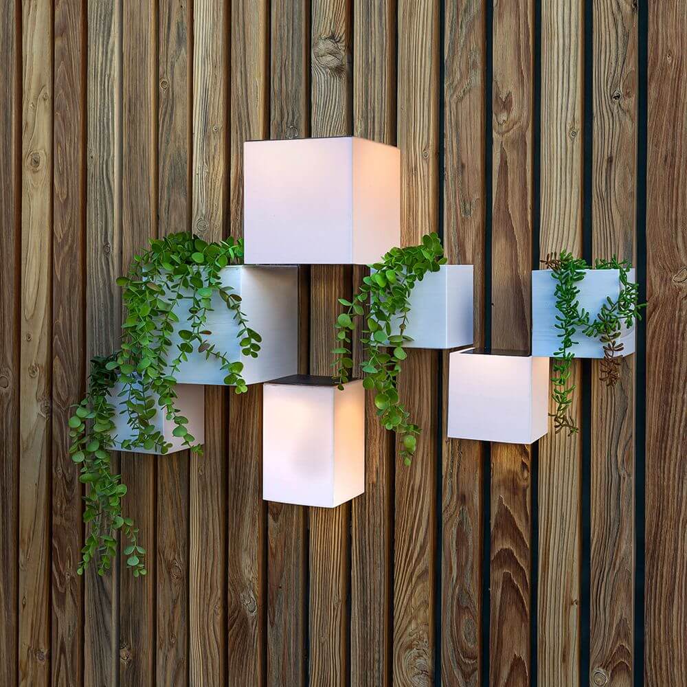 Wally LED Solar Wandlampe mit Bewegungssensor an Holzwand, elegantes Design und Pflanzen.
