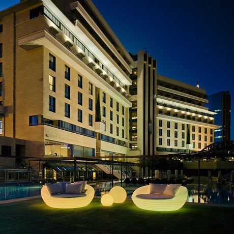 Fauteuil illuminé Formentera blanc en extérieur la nuit, entouré d’architecture moderne et d’une piscine.