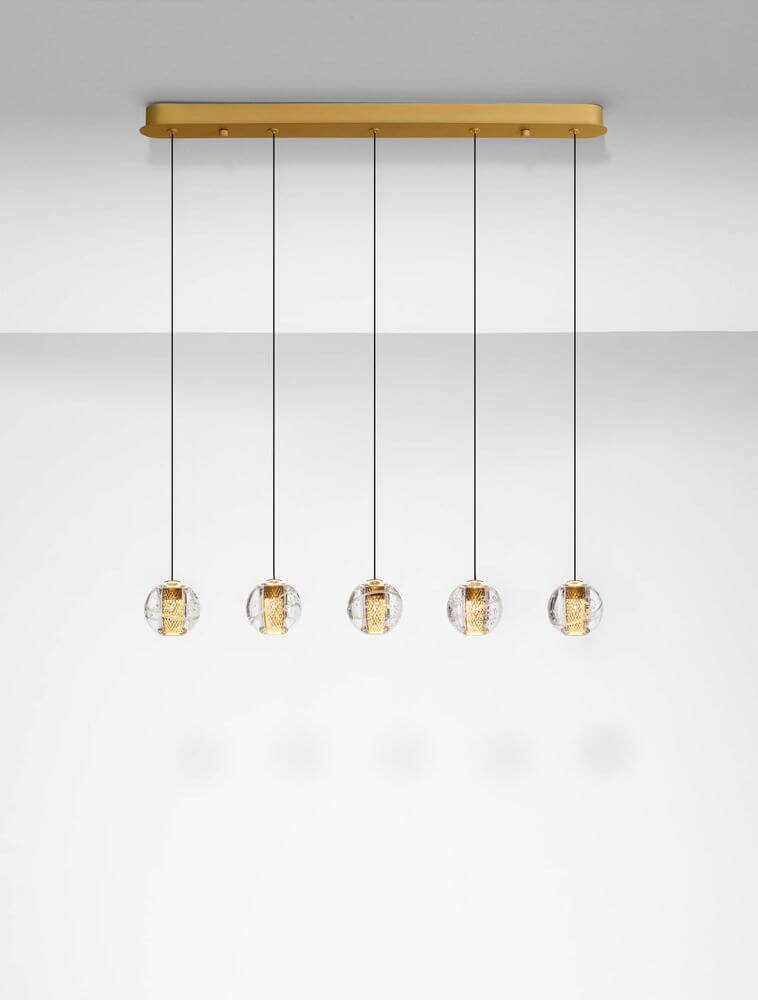 Licio Pendelleuchte Balken 84cm 5-flammig 3000K Gold in einem modernen Wohnraum, mit goldenem Aluminium und transparentem Acryl.