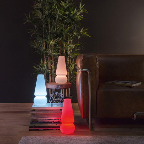 Baby Marge LED-Akkuleuchte in verschiedenen Farben neben einem gemütlichen Sofa.