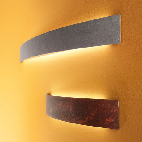 Applique murale Curvè LED Small au design moderne avec une lumière chaude sur un mur jaune.