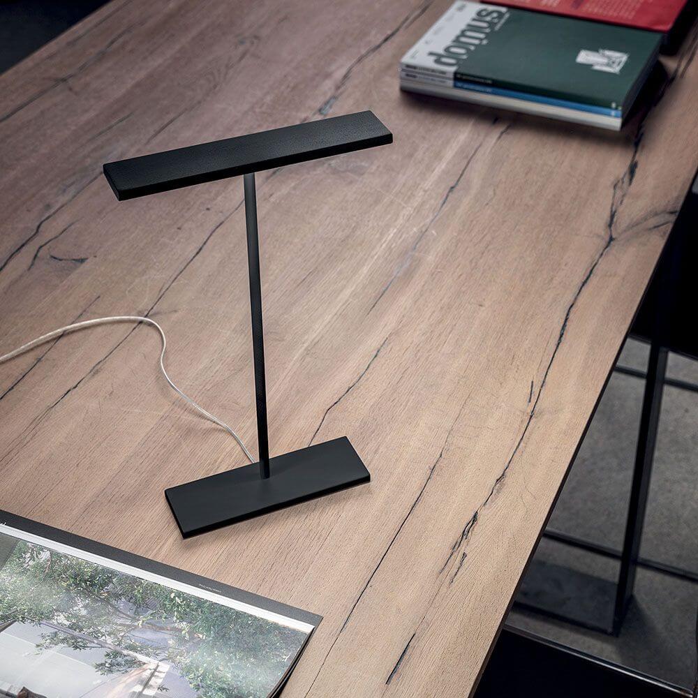 Dublight C tab LED-Tischleuchte auf einem modernen Holztisch mit Magazinen.