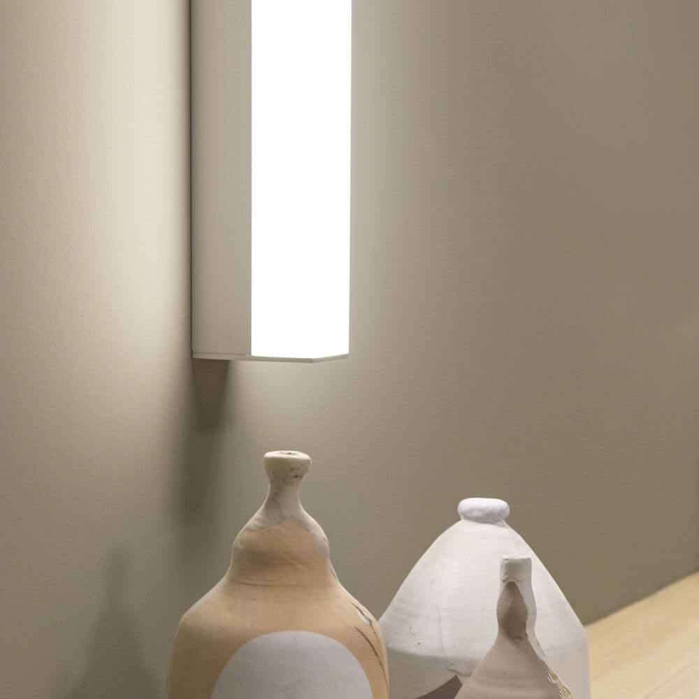 Kioo LED-Wandleuchte Mini neben dekorativen Vasen auf einem Tisch in neutralem Raum.