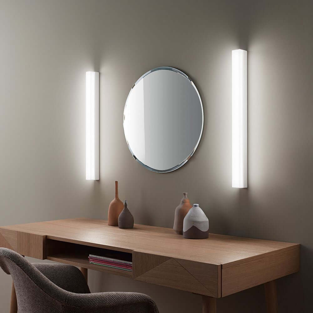 Kioo LED-Wandleuchte Mini neben einem runden Spiegel über einem modernen Holztisch.