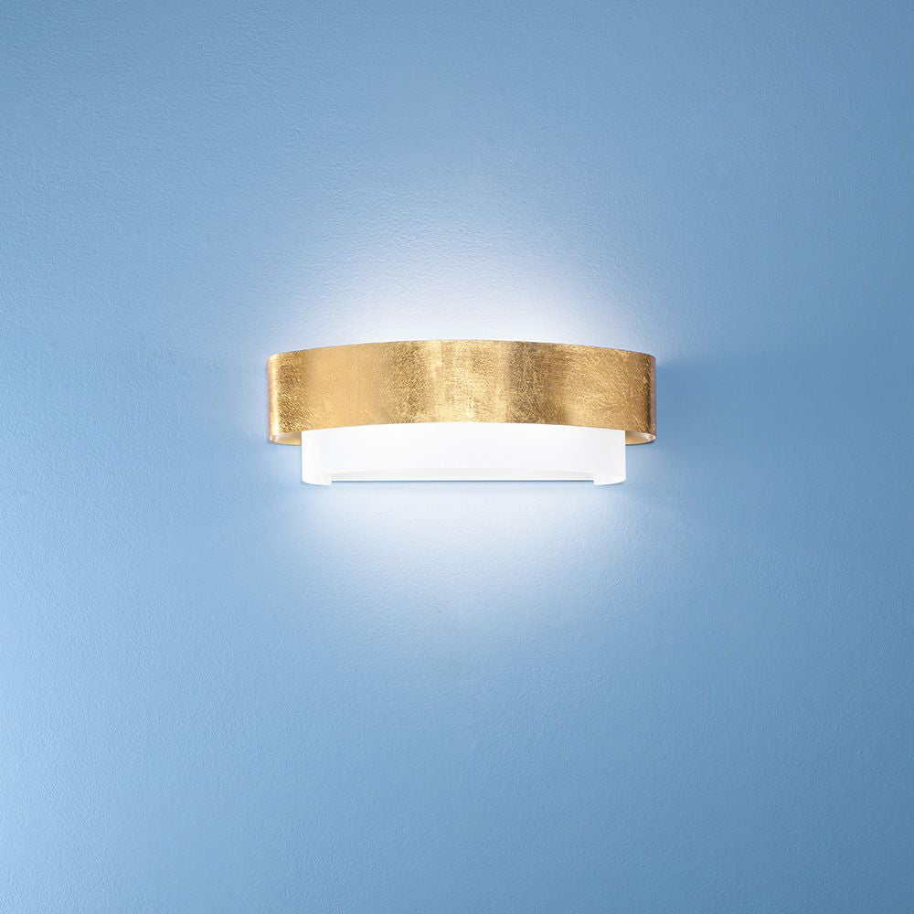 Matrioska W Wandleuchte Big an einer blauen Wand, kombiniert goldene und weiße Elemente.