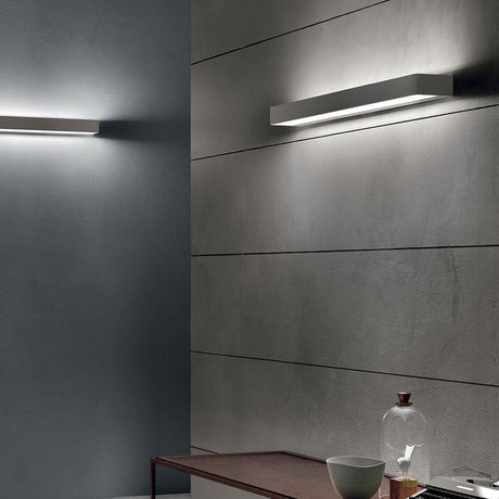 Moderne Einrichtung mit Metal W LED-Wandleuchte Large an der Wand und stilvollem Tisch mit Dekoration.