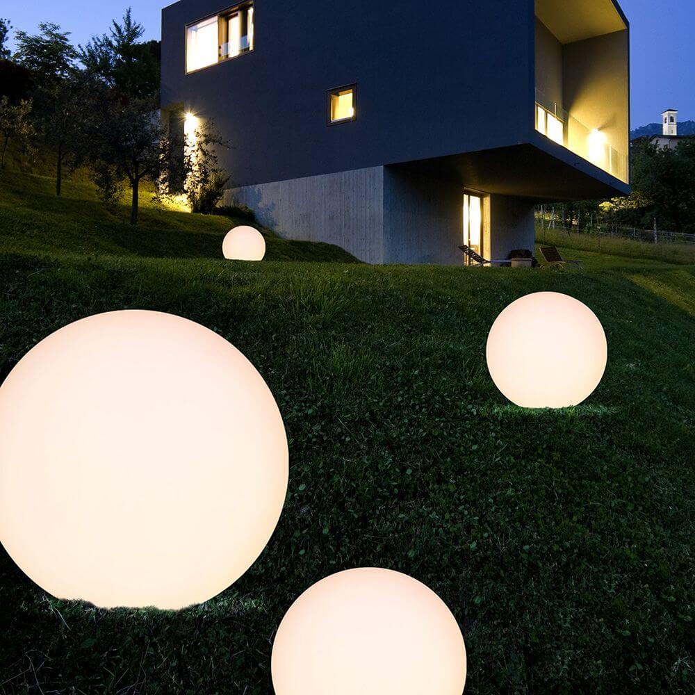 Oh! FL65 LED-Bodenleuchte im Garten mit leuchtenden, runden Lampen vor modernem Gebäude.