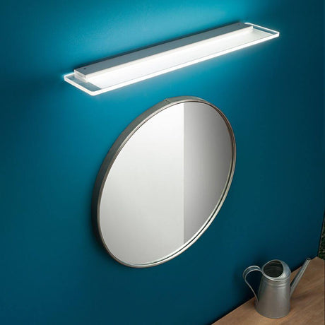 Skinny LED-vegglampe Small over rund speilflate på blå vegg.