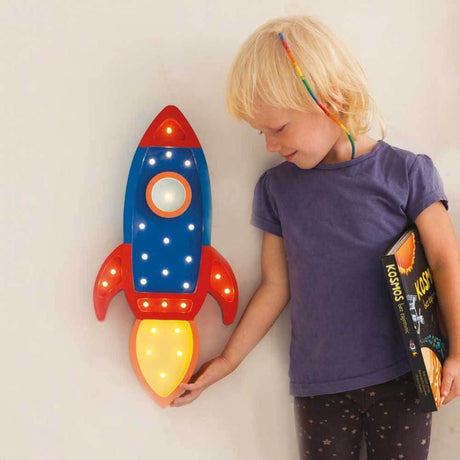 Kinder Wand- & Tischleuchte Rakete mit einem Kind, das die Lampe betrachtet und ein Buch hält.