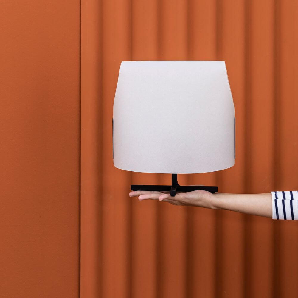 Luang Tischleuchte in Hand gehalten vor oranger Wand.