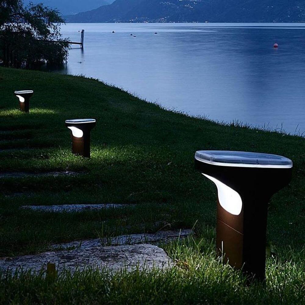 Luceplan Außen-Bodenleuchte Sky IP65 28cm in einem Garten am Wasser, stilvoll beleuchtet in der Dämmerung.