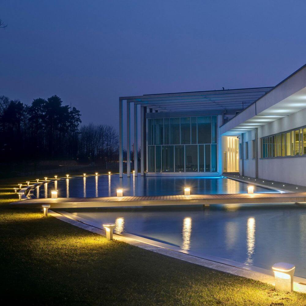 Moderne Luceplan Sky Außenlampe beleuchtet den Weg entlang eines Pools bei Nacht.