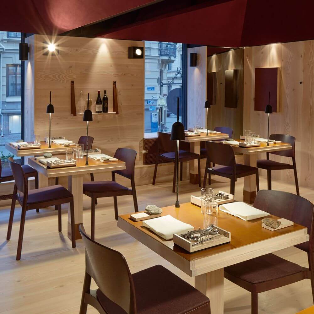 Innenansicht eines modernen Restaurants mit Tischen und Stühlen, beleuchtet von eleganten Lampen.