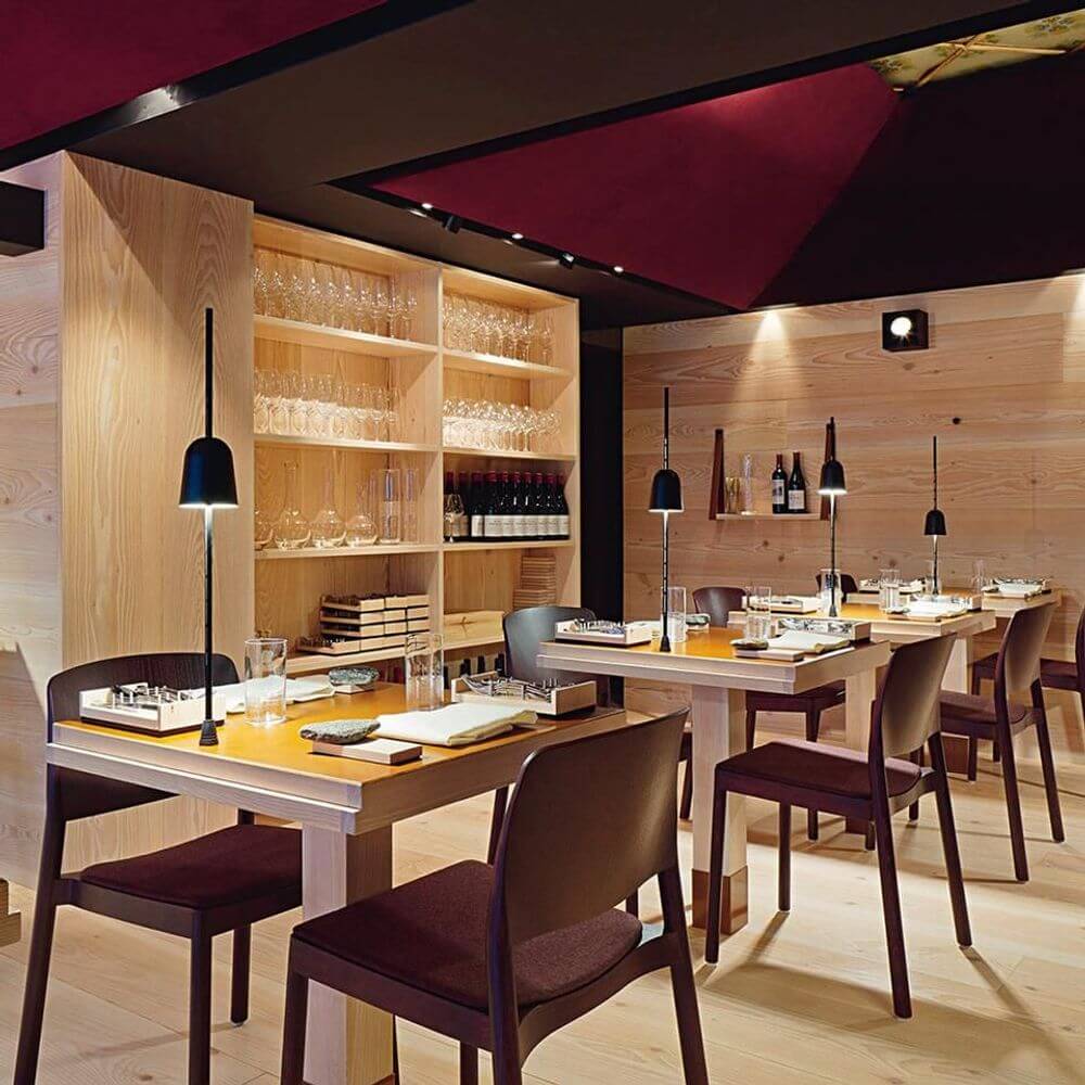 Moderne Einrichtung eines Restaurants mit Luceplan LED Schreibtischlampe Ascent schwarz auf den Tischen.