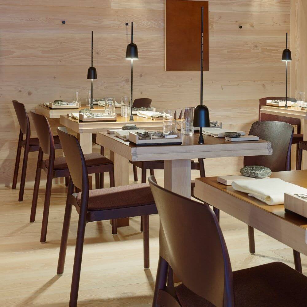 Moderne Restaurantanordnung mit Luceplan LED Schreibtischlampe Ascent schwarz und eleganten Holzstühlen.