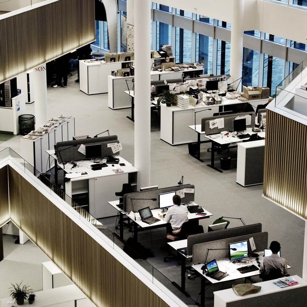 Büroszene mit mehreren Arbeitsplätzen, modernen Schreibtischen und Laptops in einer offenen Büroumgebung.