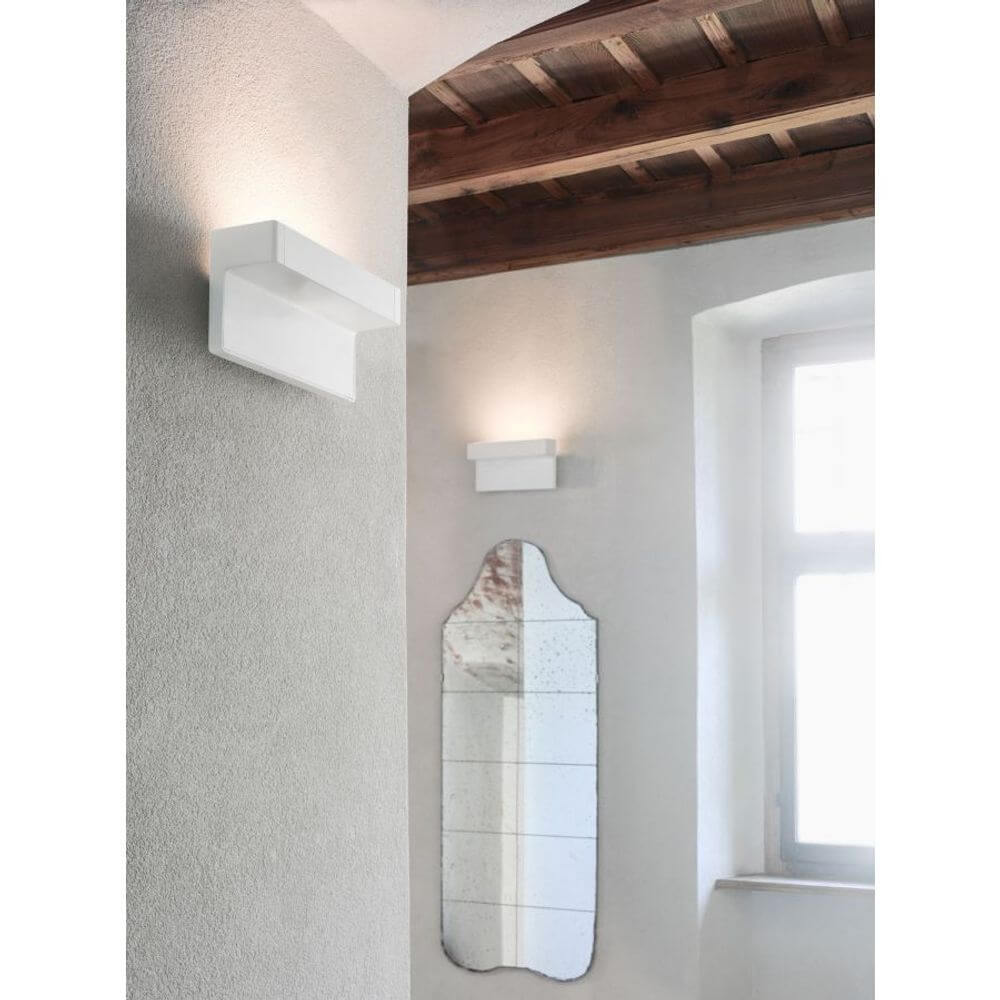 Luceplan LED Wandleuchte Any 23cm weiß an einer Wand, freundlich beleuchtet neben einem Spiegel.