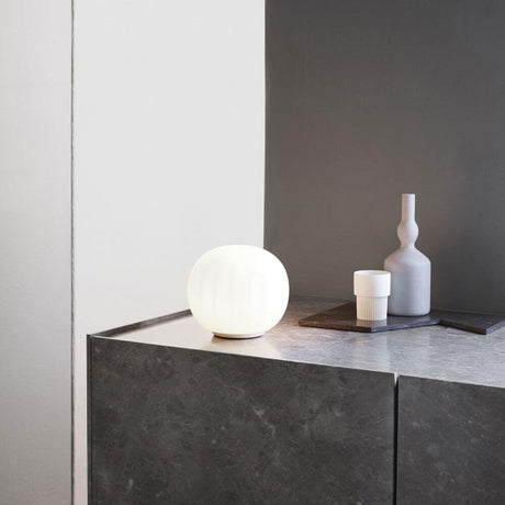 Luceplan Lita Tischlampe Ø 14cm Opal auf einer modernen Tischoberfläche mit dekorativen Objekten.