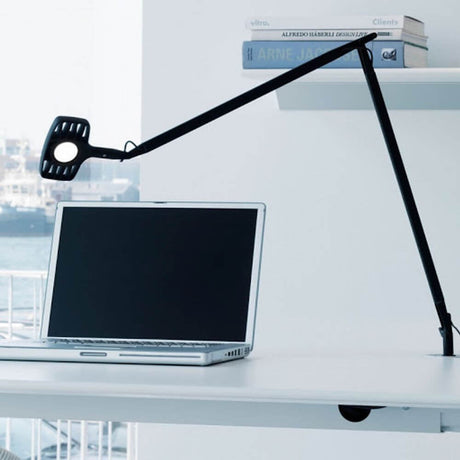 Luceplan Otto Watt Tischklemme mit dimmbarem LED-Licht auf einem Schreibtisch neben einem Laptop.