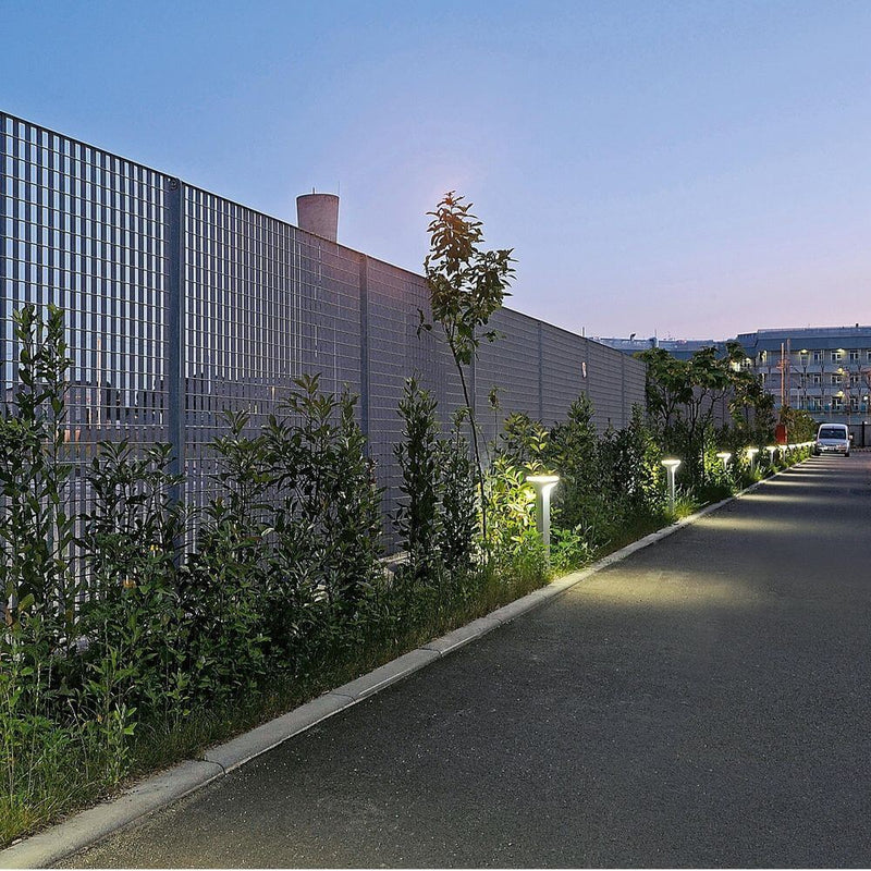 Borne lumineuse Luceplan Sky 70 cm IP65 éclairant un chemin moderne le long d’une clôture au crépuscule.