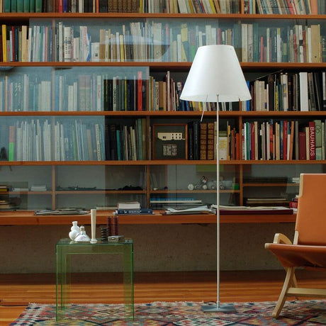 Lampadaire Luceplan Costanza avec variateur à capteur D13 c dans un espace de vie moderne avec étagère à livres et fauteuil.
