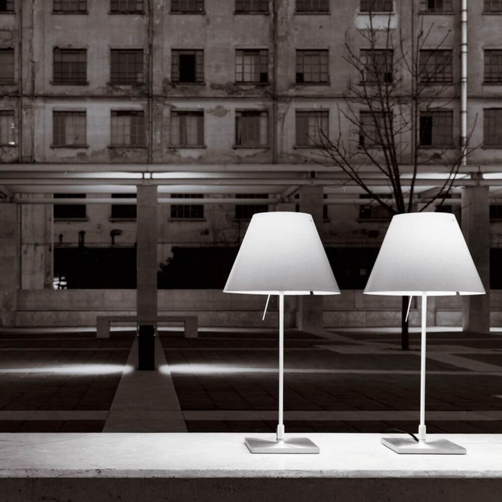Zwei Luceplan Stehlampe Costanza mit Sensor-Dimmer D13 c in einer urbanen Umgebung bei Nacht.