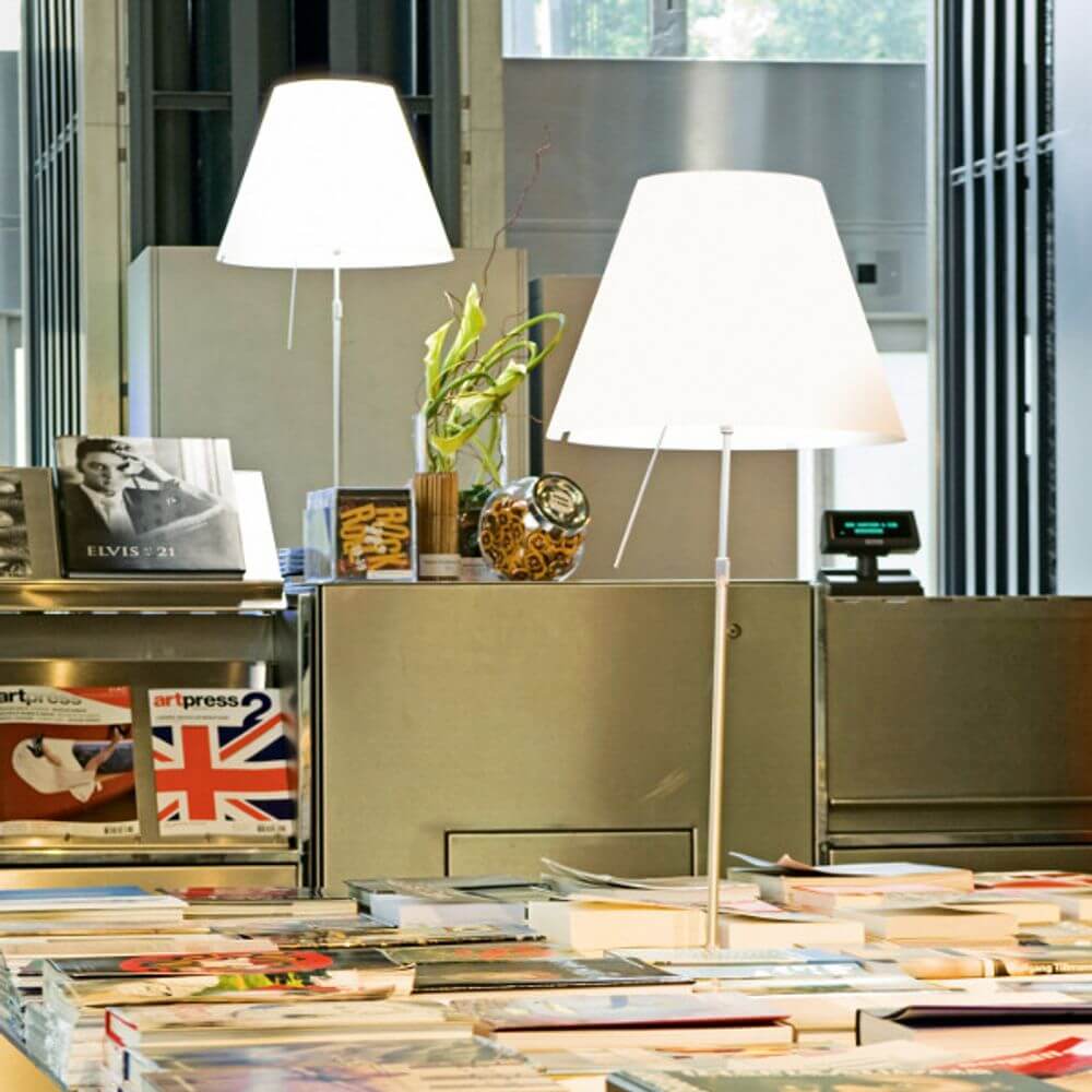 Luceplan Stehlampe Costanza mit Sensor-Dimmer D13 tc beleuchtet einen Tisch mit Zeitschriften.