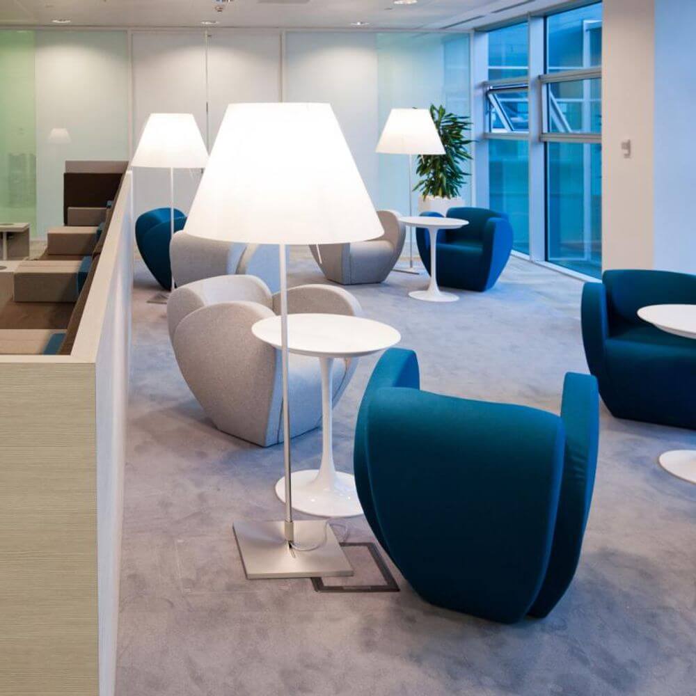 Luceplan Stehlampe Grande Costanza mit Sensor-Dimmer in modernem Büroraum mit gemütlichen Sitzgelegenheiten.
