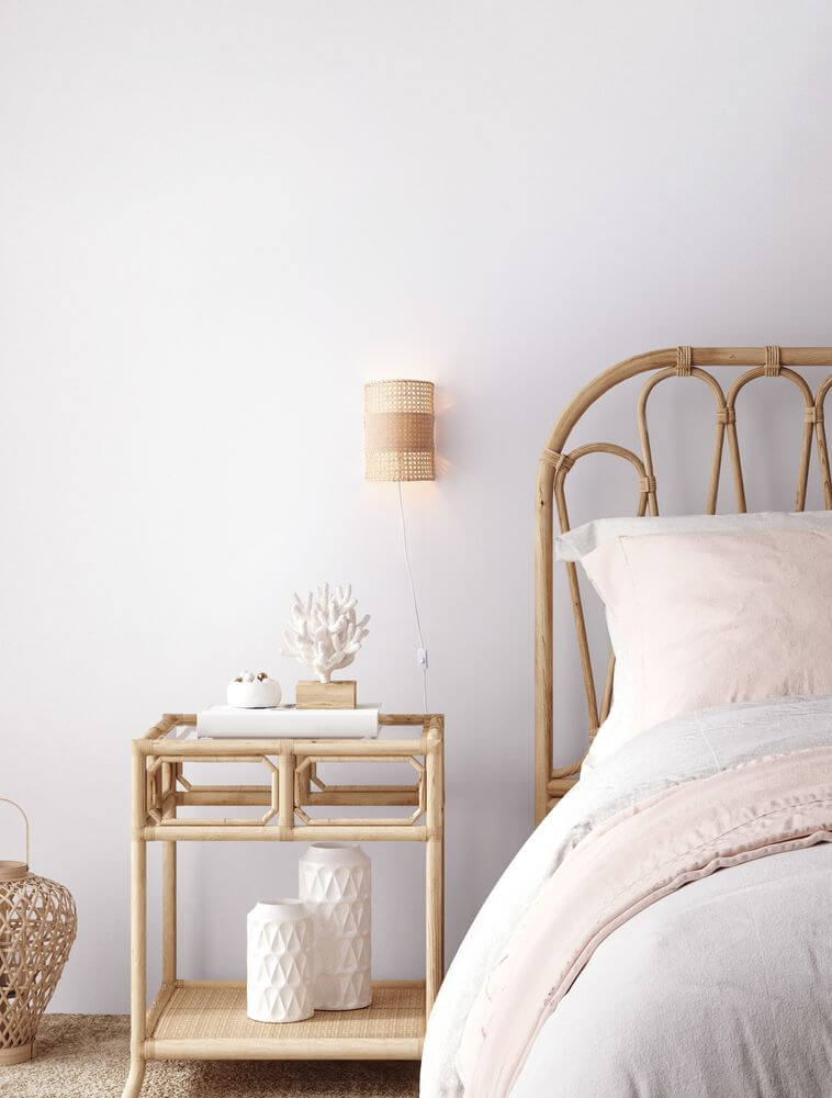 Lum Wandleuchte Natur mit Rattan-Design neben einem Bett in einem hellen Schlafzimmer.