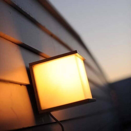 Lutec Außen-Wandleuchte Box Cube IP54 Anthrazit an einer Wand, warmes Licht strahlt durch den frosted Diffusor.
