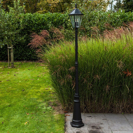 Lutec London Außen-Standleuchte IP44 300lm im Garten mit hohem Gras und schwarzer Aluminiumkonstruktion.