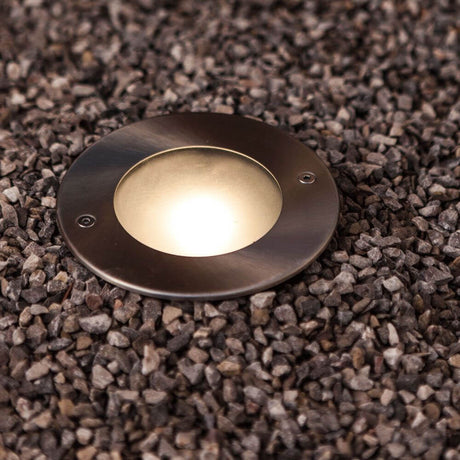 Lutec Strata stainless steel round recessed floor spotlight IP67 320 lm on gravel ground, ideal for terrace lighting.