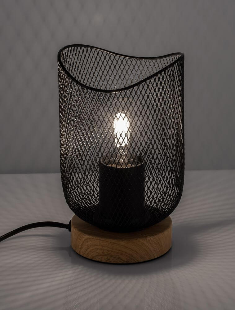 Lyron Tischleuchte E27 Ø 12cm mit schwarzem Metallkorb und Naturholzfuß auf einem Tisch.
