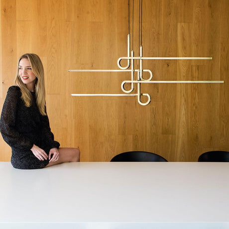 Cinto 4-flammig geschwungene LED-Hängeleuchte 4-flammig über einem minimalistischen Tisch mit einer Frau im eleganten Outfit.