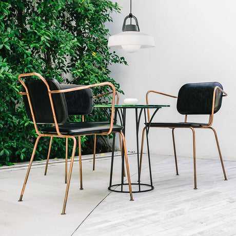 Modern Kinke pendant lamp above an elegant table with chairs in a green setting.