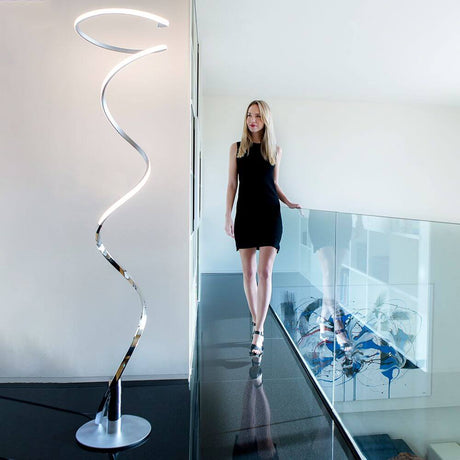 Helix geschwungene LED-Stehleuchte in modernem Wohnzimmer neben Frau in schwarzem Kleid, geschwungene Metallform und indirekte LED-Beleuchtung