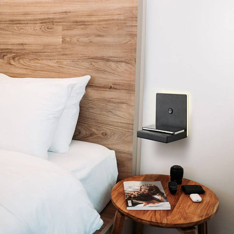Zanzibar quadratische LED-Wandleuchte mit Ladestation an einer Schlafzimmerwand neben einem Nachttisch.