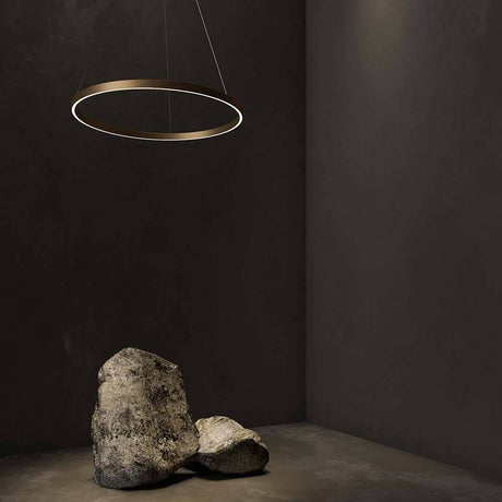 Rim LED Ring Pendellampe in Messing, modernes Design in einem minimalistischen Raum mit Steinen.