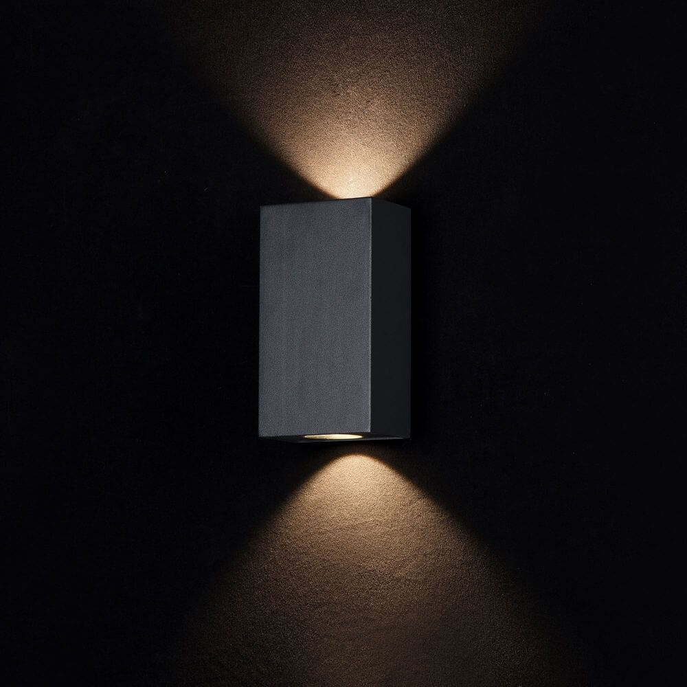 TimesSquare LED-Außenwandlampe Small IP54 an einer dunklen Wand mit sanfter Beleuchtung.