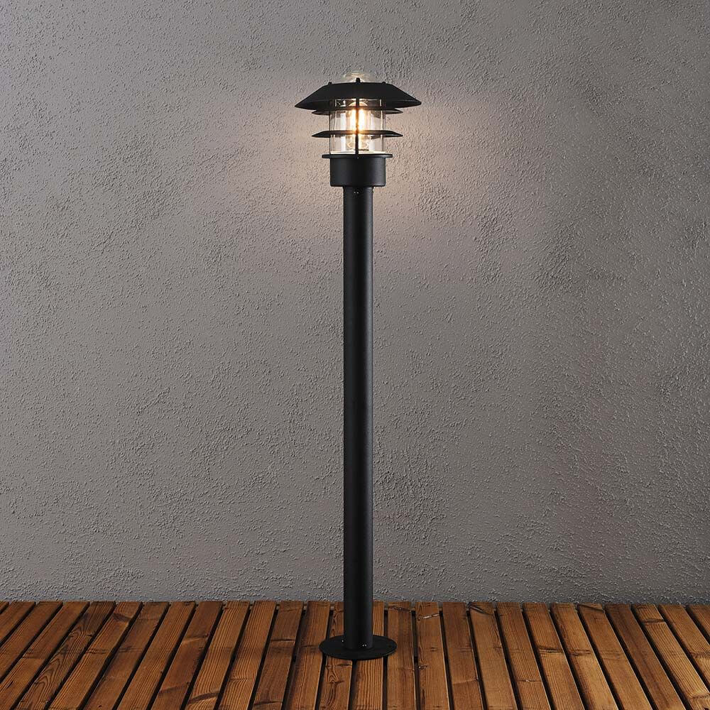Modena Wegeleuchte Schwarz, klares Glas auf Holzterrasse mit warmem Licht.