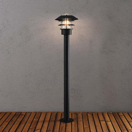 Modena Wegeleuchte Schwarz, klares Glas auf Holzterrasse mit warmem Licht.