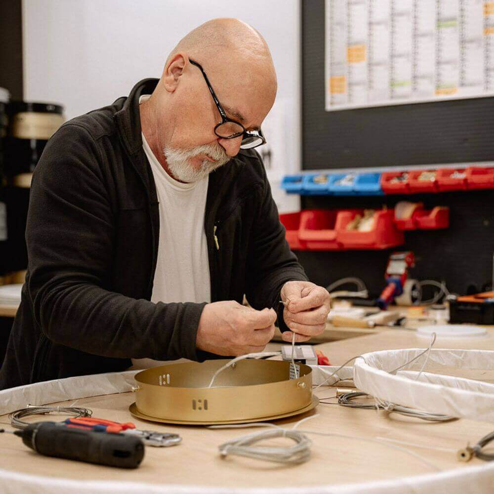 Ein Handwerker arbeitet an einer Lampe und verbindet Kabel in einer Werkstatt.