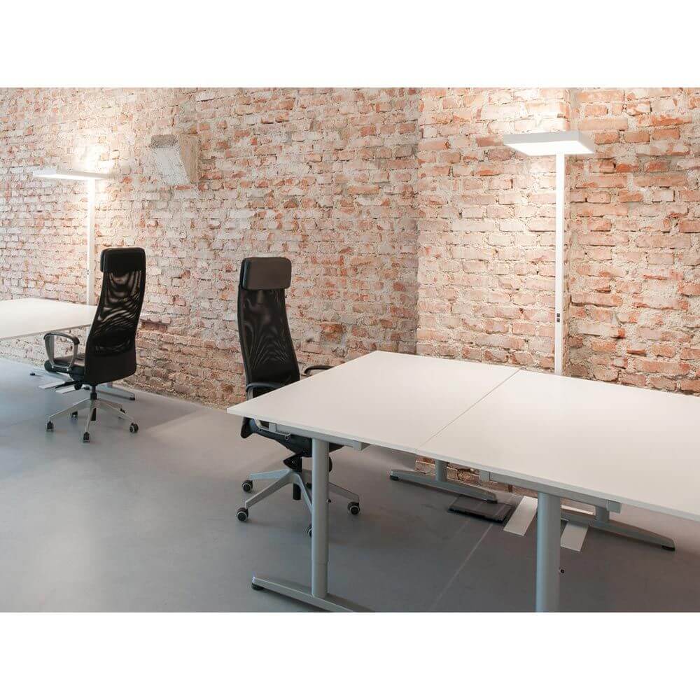 Moderne Büroeinrichtung mit System Büro Stehleuchte Push-Dim Grau und schwarzen Drehstühlen vor einer Ziegelwand.