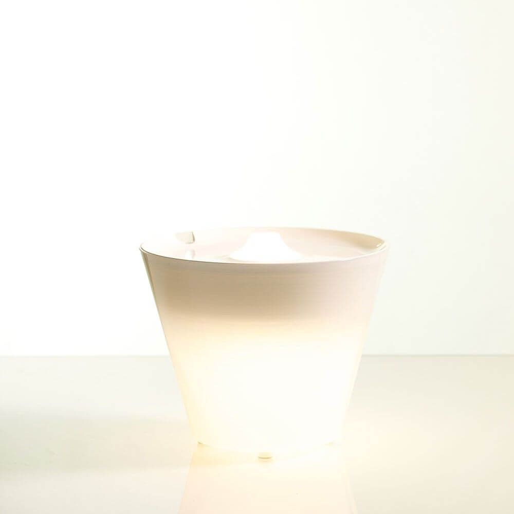 Rotaliana Multipot+ table lamp cable container + charging station white in minimalist design, softly glowing.