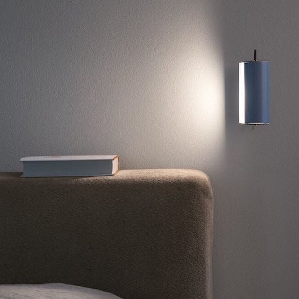Nemo Applique Cylindrique Petite Wandlampe 16cm an einer Wand neben einem Bett mit einem Buch.